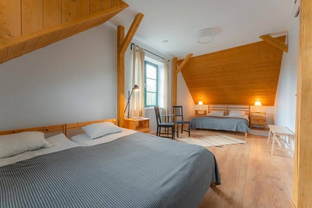 Une chambre avec deux lits, un bureau, une chaise, une fenêtre avec des rideaux et des poutres en bois.