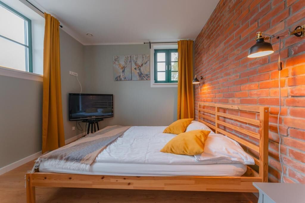 A bedroom with a wooden bed, a television, a brick wall, and a window with curtains.