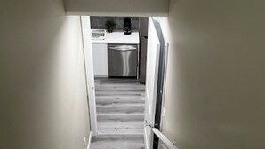 Una escalera conduce a una cocina con un refrigerador de acero inoxidable y una pequeña planta en maceta sobre la encimera.
