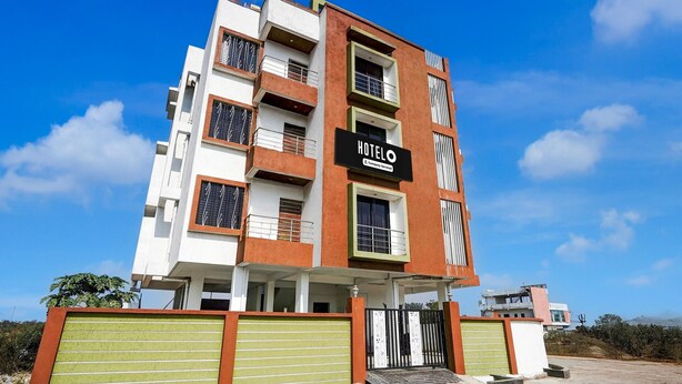 Un hôtel à plusieurs étages, reconnaissable à son grand panneau lumineux indiquant « HÔTEL », à ses balcons et à son entrée sécurisée par un portail.