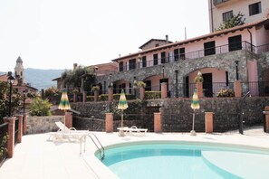 A swimming pool with lounge chairs and umbrellas, surrounded by stone walls and buildings with balconies. - Apartment in Casanova Lerrone (Casanova Lerrone)