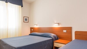 Ein Hotelzimmer mit zwei Betten, einem Nachttisch, einer Wandleuchte und einem Fenster mit Vorhängen.