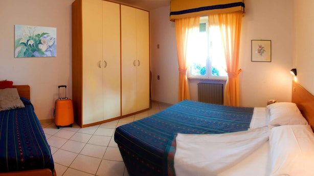 Ein Hotelzimmer mit einem Bett, einem Kleiderschrank, einem Koffer und einem Fenster mit Vorhängen.