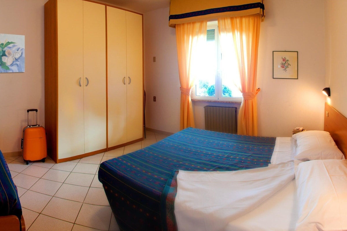 Ein Hotelzimmer mit zwei Betten, einem Schrank, einem Koffer und einem Fenster mit Vorhängen.