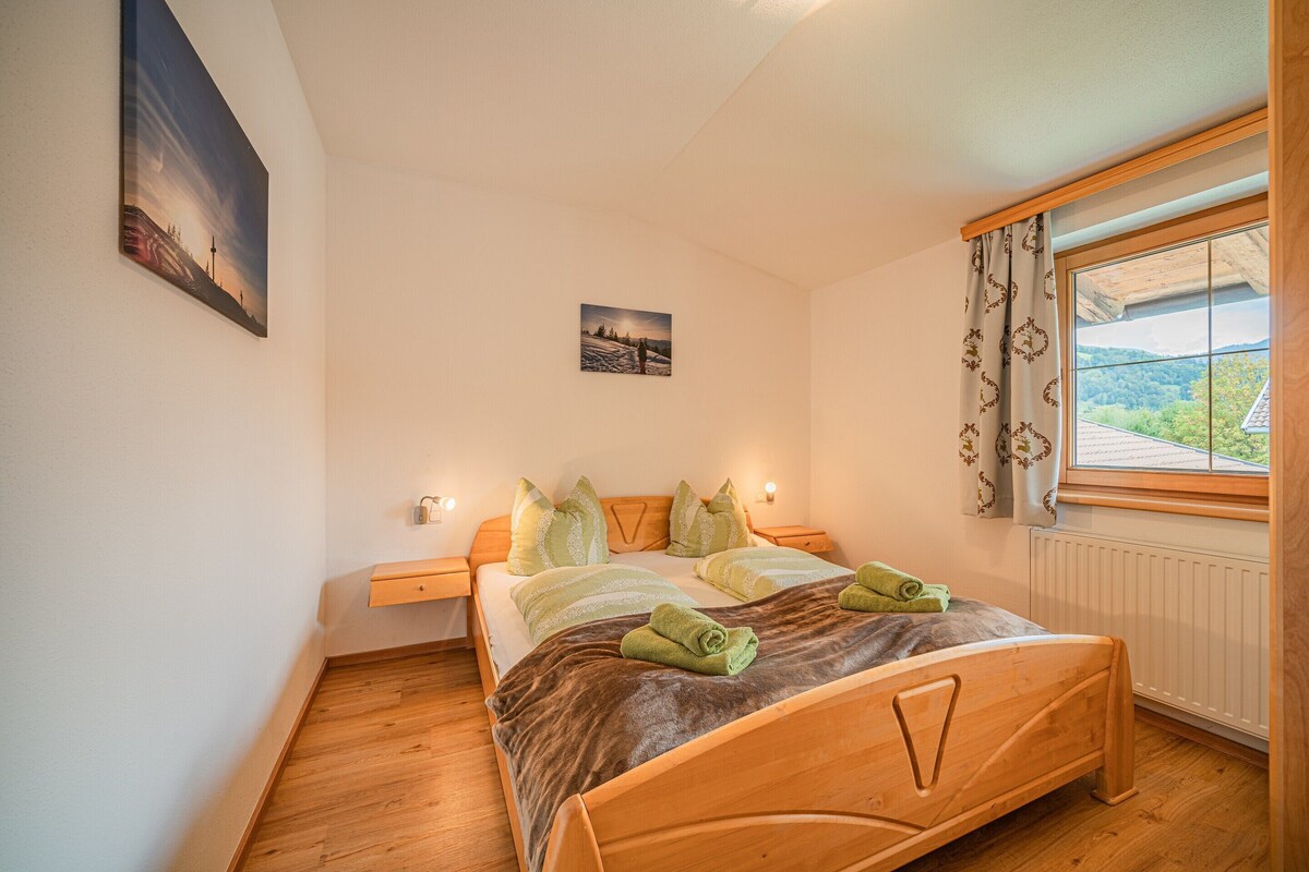 Un dormitorio con una cama de madera, una mesita de noche, una ventana con cortinas y un cuadro en la pared.