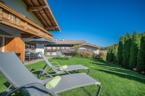 A hotel with a wooden facade, outdoor seating area with lounge chairs, and a well-maintained lawn. - Apartment in Brixen Near Wilder Kaiser Gondola (Brixen im Thale)