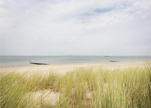 A beach with sand and grass, a boat in the water, and a distant shoreline. - Apartment in Groede Near the Beach (Groede)