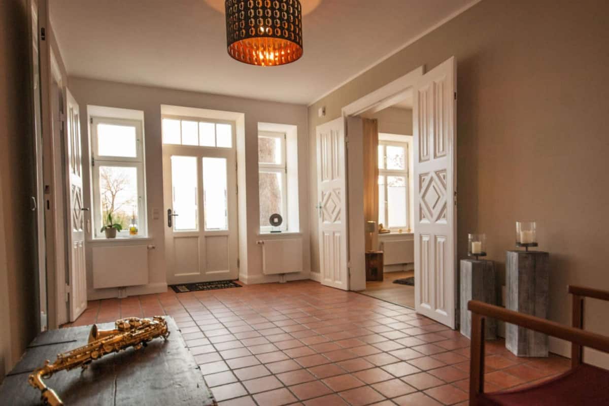 Una habitación amplia con ventanas grandes, suelo de madera y una lámpara de techo original.