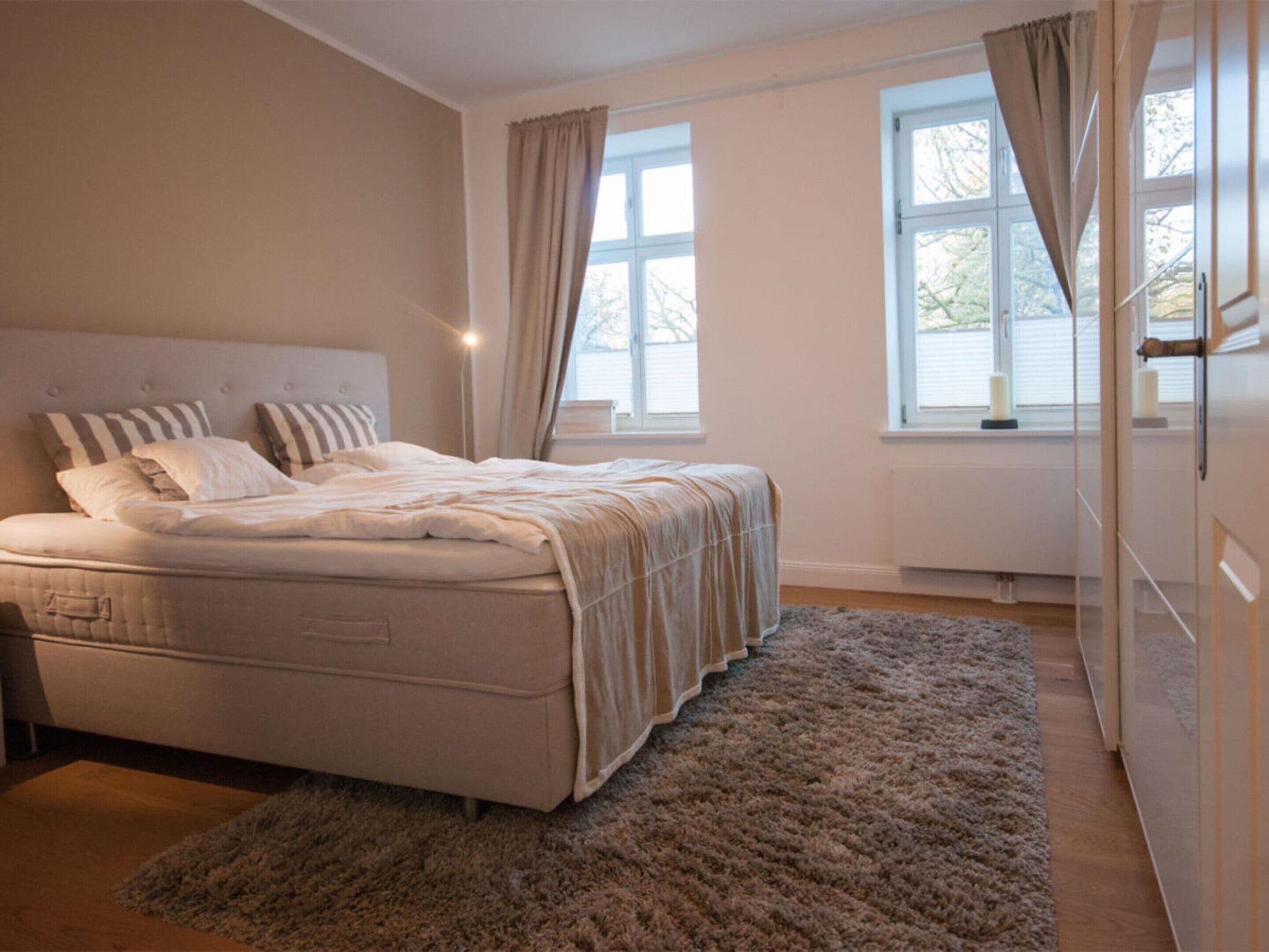 A bedroom with a bed, a window with curtains, a radiator, and a door.
