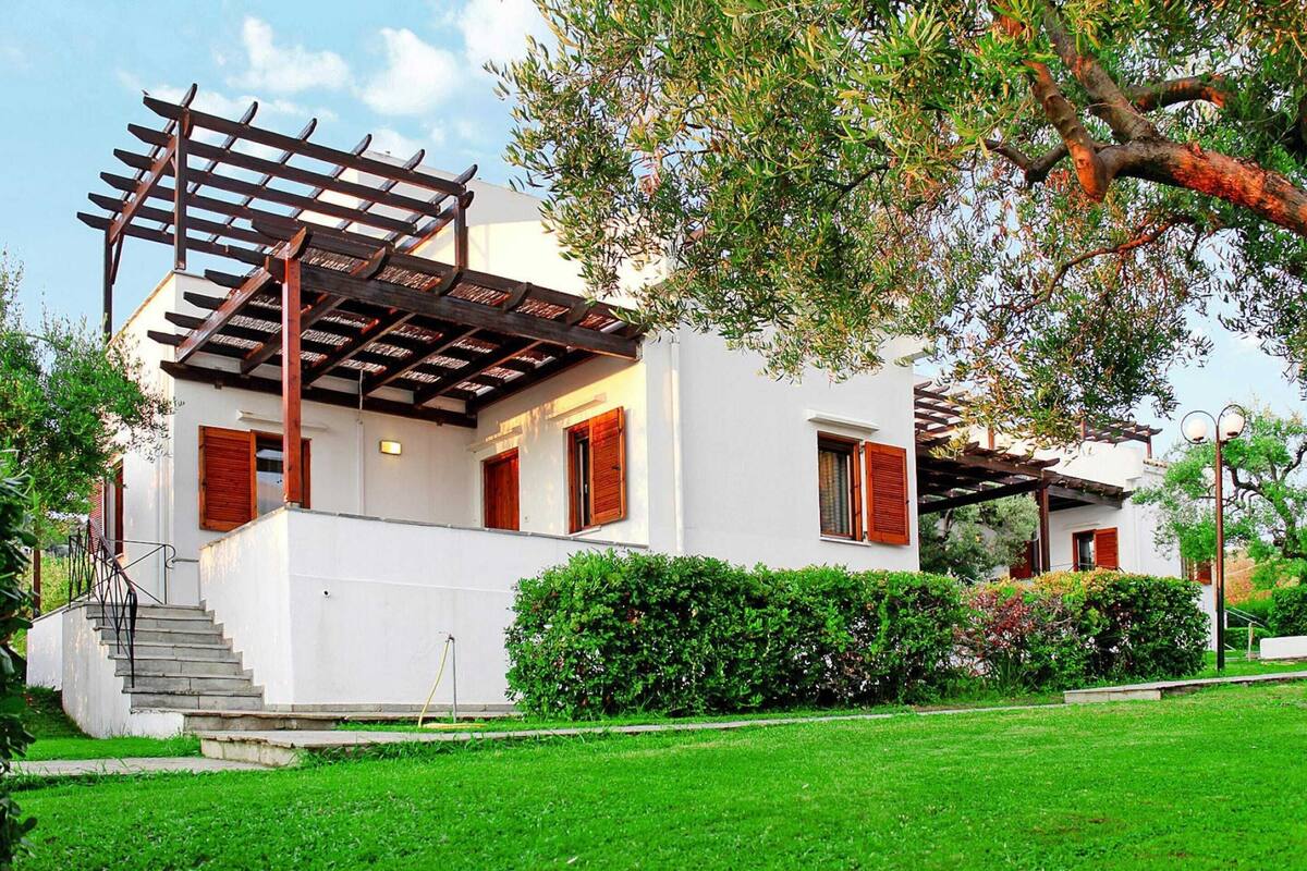 A modern two-story house with a wooden pergola, a staircase, and a well-maintained lawn.