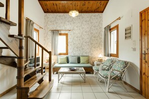 Ein Wohnzimmer mit einer Holztreppe, einem Sofa, einem Couchtisch, Korbstühlen und einer Holzbalkendecke.
