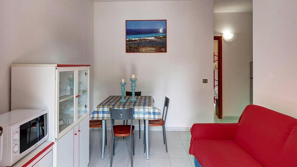 A compact living space with a dining area, a red sofa, a microwave, and a painting on the wall. - Apartment in San Teodoro (San Teodoro)