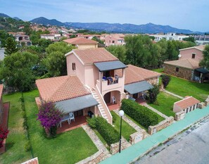 Ein zweistöckiges Haus mit Balkon, umgeben von einem gepflegten Garten und Blick auf die Berge.
