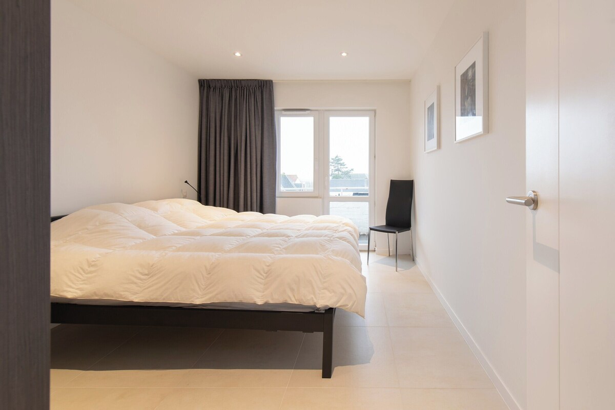 A modern bedroom with a large bed, a chair, and a TV.