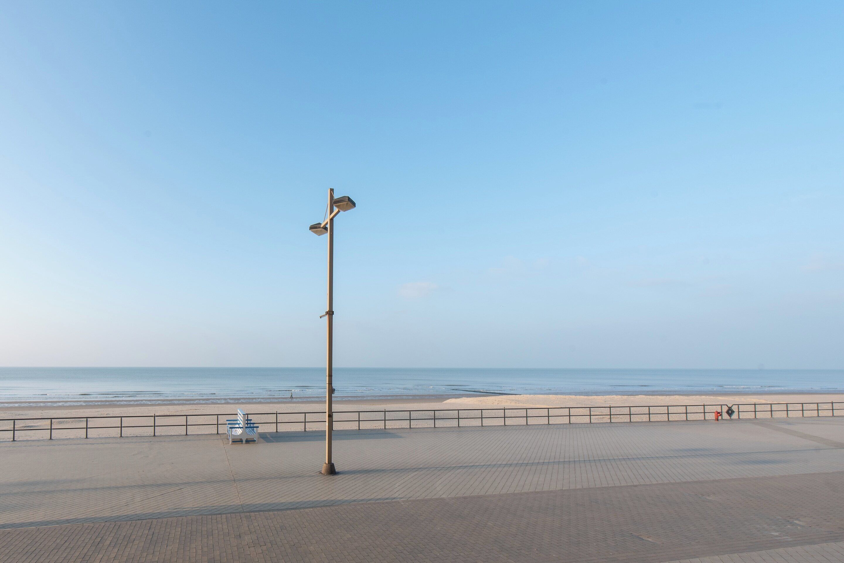 Un chemin piétonnier dallé, agrémenté d’une rambarde métallique, d’un banc et d’un lampadaire.