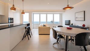 Une cuisine moderne dotée d’un îlot central, de luminaires suspendus et d’une grande fenêtre offrant une vue sur la mer.