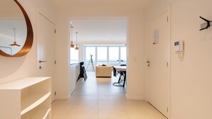 Une chambre d’hôtel moderne dotée d’un grand miroir, d’une console blanche, d’un coin repas avec une table et des chaises, et offrant une vue sur la mer grâce à de grandes fenêtres.