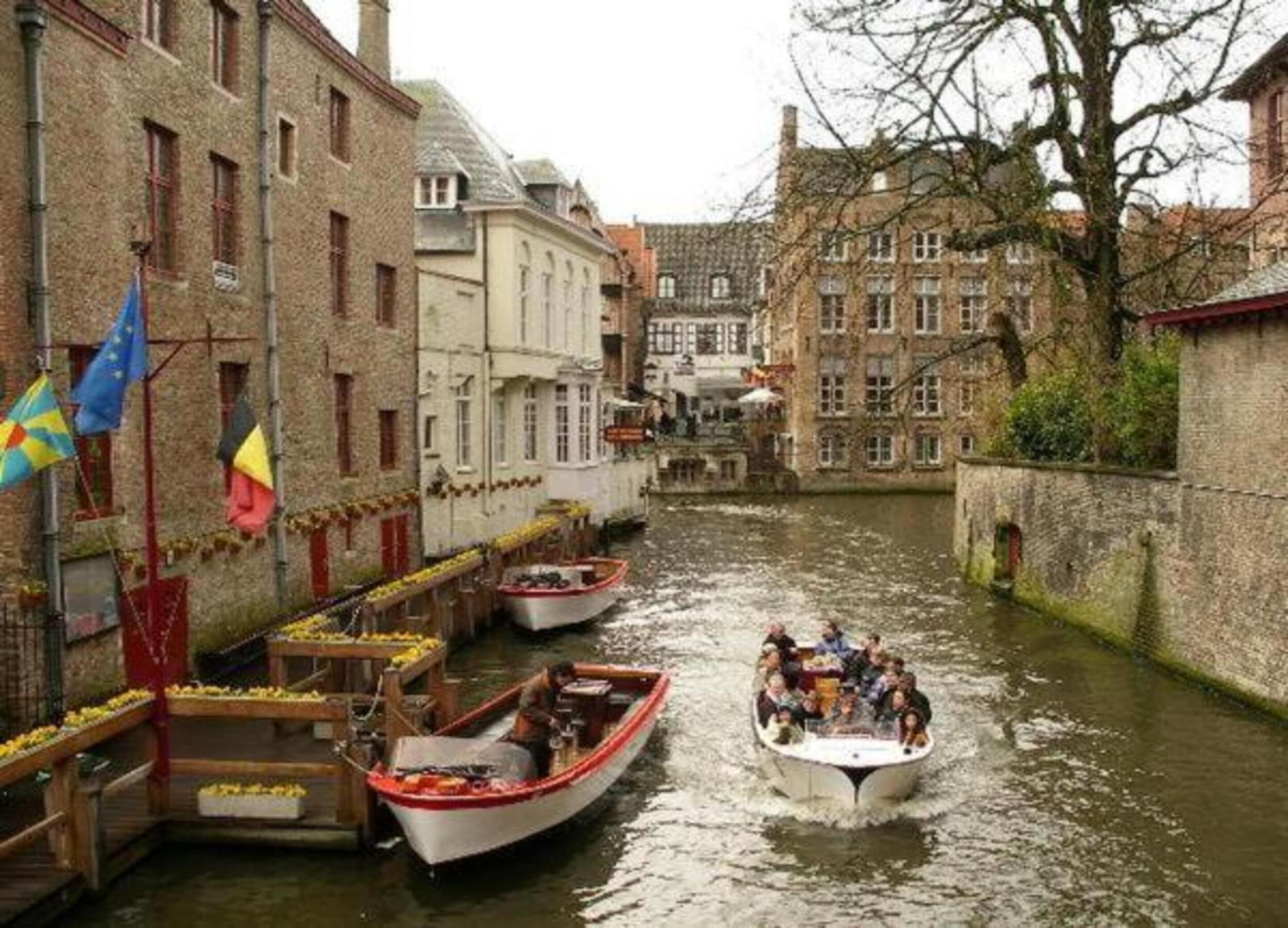A narrow canal with boats, buildings on either side, and flags.