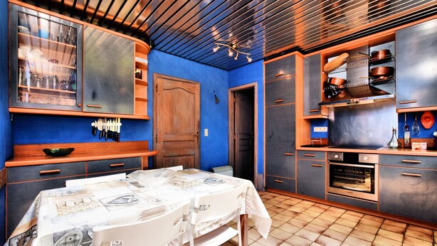 Una cocina con pared azul, armarios de madera, piso de baldosas y una zona de comedor con mesa lista para dos.