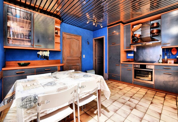 A kitchen with a blue wall, wooden cabinets, a tiled floor, and a dining area with a table set for two. - House Ardennes Blue in Theux Near Spa (Theux)