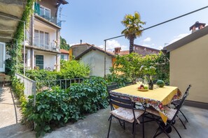 A patio with a table set for dining, surrounded by greenery and a view of neighboring buildings. - Appartamento in Centro Storico a Cannero Riviera (Cannero Riviera)