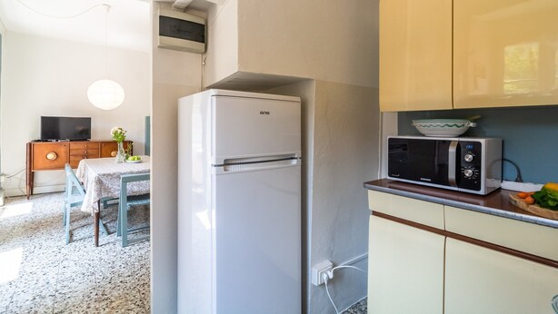A compact kitchen with a refrigerator, microwave, and a dining area with a table and chairs. - Appartamento in Centro Storico a Cannero Riviera (Cannero Riviera)