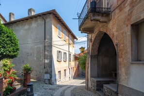 A narrow street with buildings, a brick wall, and a small garden with potted plants. - Appartamento in Centro Storico a Cannero Riviera (Cannero Riviera)