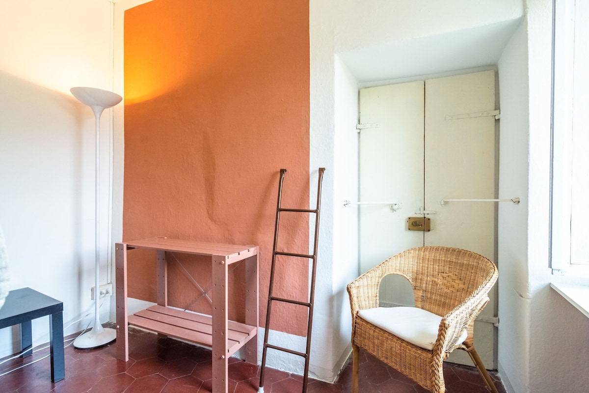 A room with a wooden ladder, a wicker chair, a white floor lamp, and a white door.