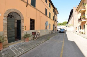 A narrow street with a building featuring an arched entrance, a bicycle, and a parked car. - Lucca Central Garden Cottage (Lucca)