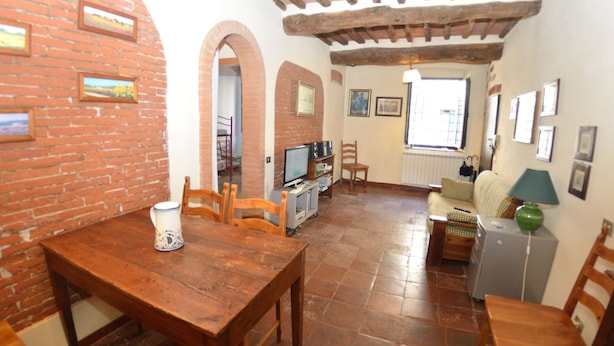 A cozy living room with a brick wall, wooden furniture, a television, and a window. - Lucca Central Garden Cottage (Lucca)