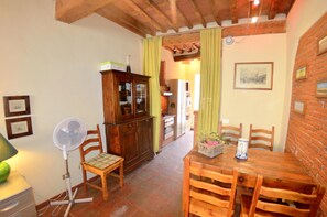 A dining area with a wooden table and chairs, a fan, a cabinet, and a brick wall. - Lucca Central Garden Cottage (Lucca)