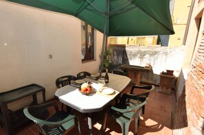 A patio with a table set for dining, chairs, a green umbrella, and a view of a building in the background. - Lucca Central Garden Cottage (Lucca)