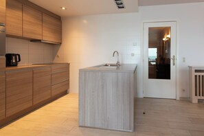 A modern kitchen with wooden cabinets, a built-in island, and a sink. - Apartment in Middelkerke With Sea View (Middelkerke)
