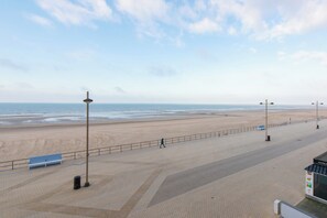 A beach promenade with a bench, street lamps, and a clear view of the ocean. - Apartment in Middelkerke With Sea View (Middelkerke)
