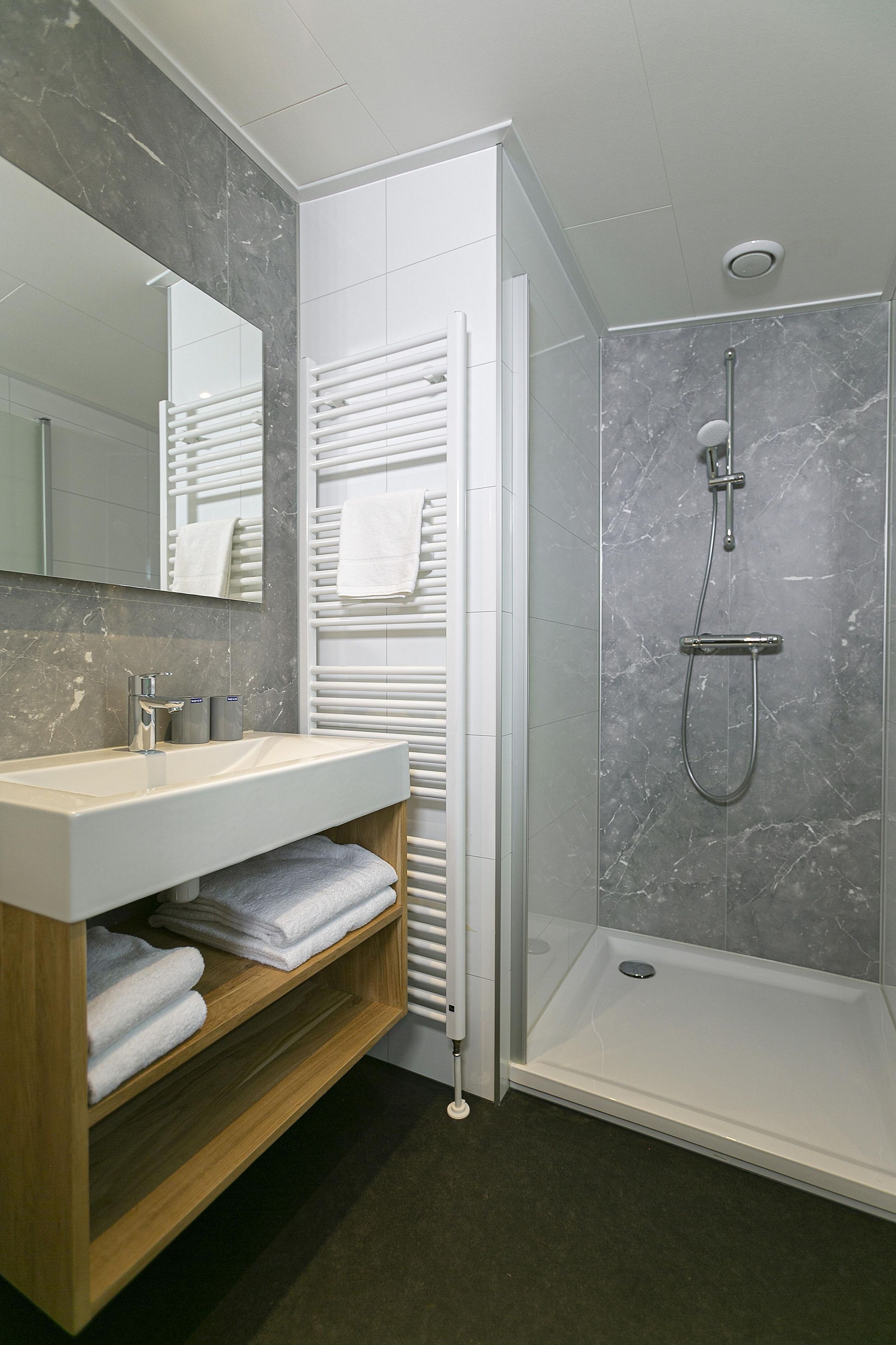 A modern bathroom with a marble shower, a white sink, and a wooden vanity.