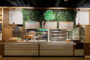 Un comptoir où l’on peut acheter des aliments, avec une pancarte indiquant « Produits frais du jardin », des panneaux affichant les menus pour les salades, les sauces, les wraps aux légumes frais, les sandwichs et les sushis.