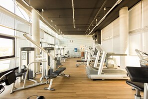 Une salle de sport équipée de divers appareils d’exercice, dotée de grandes fenêtres et d’un plancher en bois.