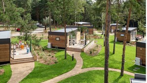 A campsite with multiple wooden cabins, a paved walkway, and a grassy area with trees. - Mobile Home im Tropical Islands Resort (Halbe)