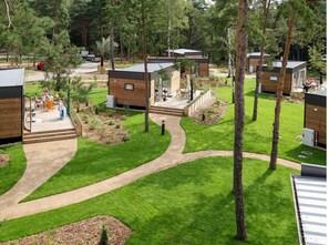 A campsite with multiple wooden cabins, a paved walkway, and a grassy area with trees. - Mobile Home im Tropical Islands Resort (Halbe)