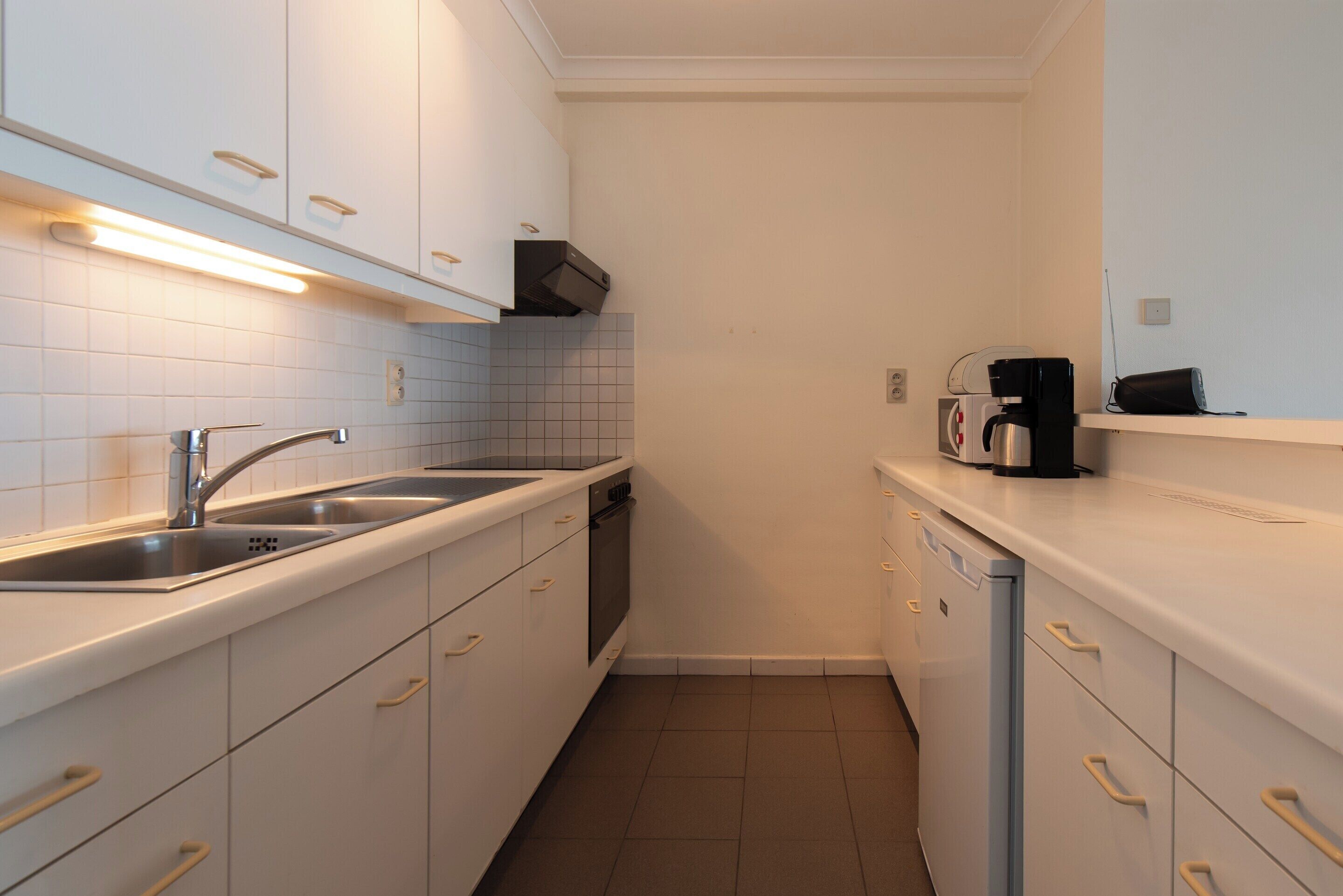A compact kitchen with white cabinets, a stainless steel sink, a coffee maker, and a dishwasher.