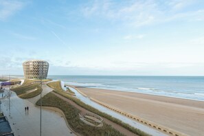 Blick auf die Küste mit einem markanten kreisförmigen Gebäude, einem Strand und einem gepflasterten Weg.