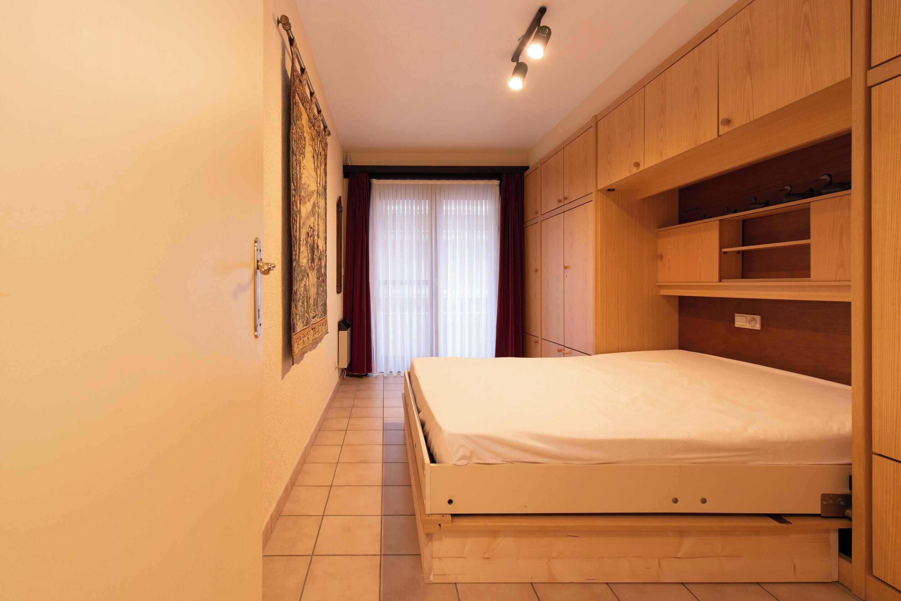 A bedroom with a wooden bed, built-in shelving, and a sliding door leading to a bathroom.