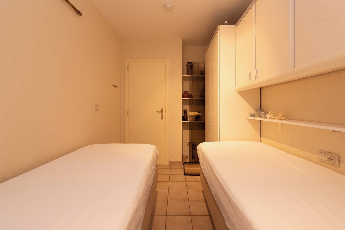 A narrow hotel room with two single beds, a wardrobe, and a small closet.
