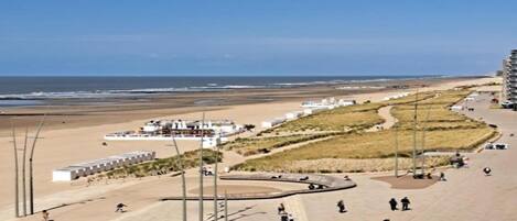 Une promenade en bord de mer, avec une plage, une rangée de bâtiments blancs et quelques personnes qui se promènent.