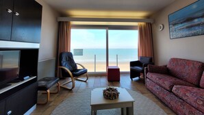 A living room with a TV, a sofa, a chair, a coffee table, and a view of the beach. - Steps From the Quiet Seaside Path (Middelkerke)