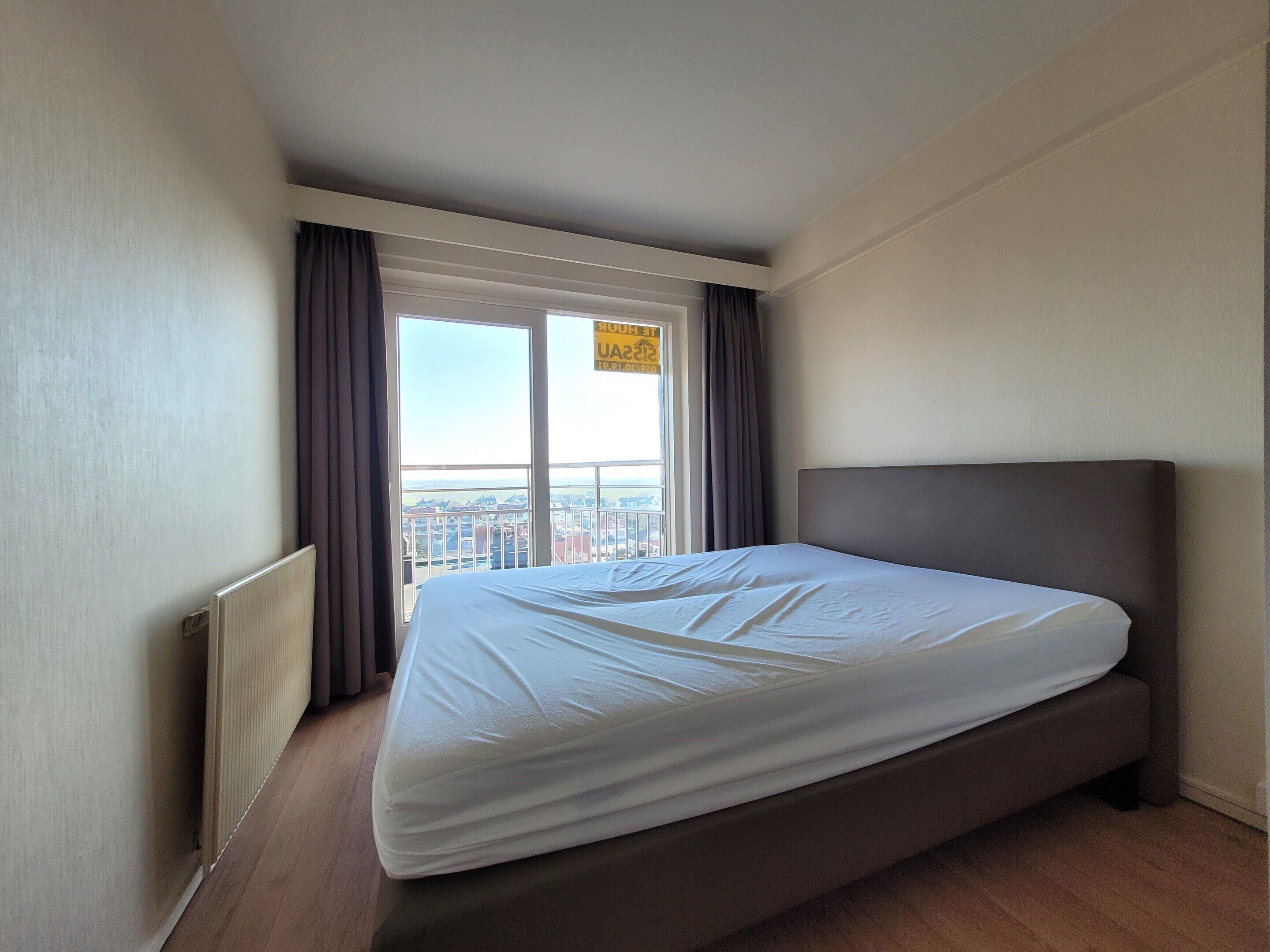A hotel room with a large bed, a window with curtains, and a view of the city.