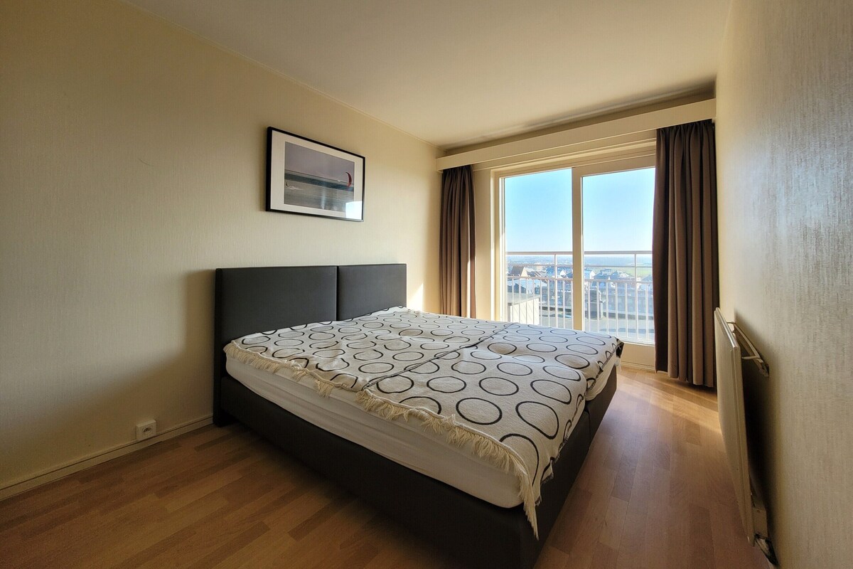 A bedroom with a large bed, a window with curtains, and a framed picture on the wall.