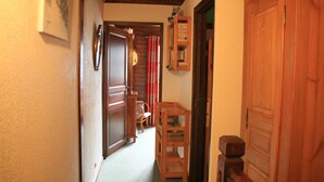 A narrow hallway with wooden doors, a wooden cabinet with books, and a chair in the background. - Apartment With Parking for 6 People (Chatel)