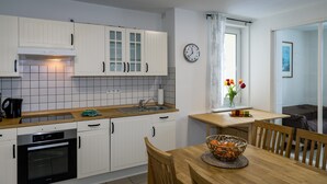 Een moderne keuken met witte kasten, een inbouwoven, een spoelbak en een eethoek met een houten tafel en stoelen.