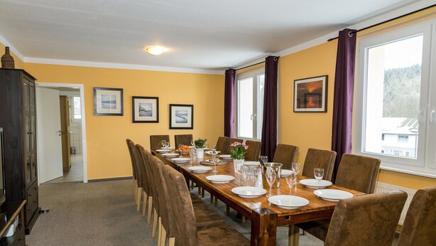 Een eetkamer met een lange tafel voor zes personen, stoelen en een kast.